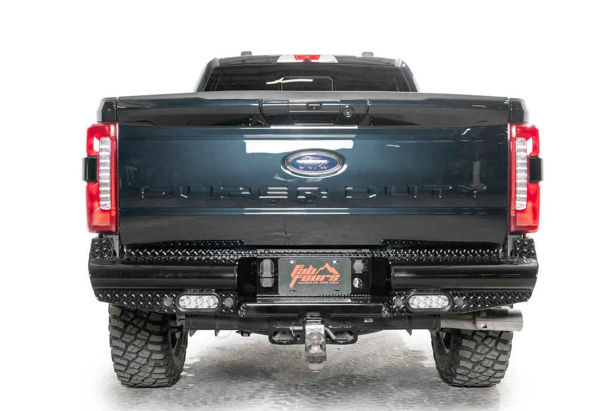 Fab Fours Black Steel rear bumper on a gray and dark blue two-tone Ford Super Duty, straight-on rear view, showing the diamond-plate face, center license plate pocket and twin LED pod lights