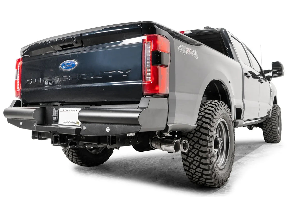 Fab Fours Black Steel Elite rear bumper on a gray and dark blue two-tone Ford Super Duty, rear passenger-side three-quarter view, showing the smooth-plate tubular profile, wrapped corners and exhaust clearance