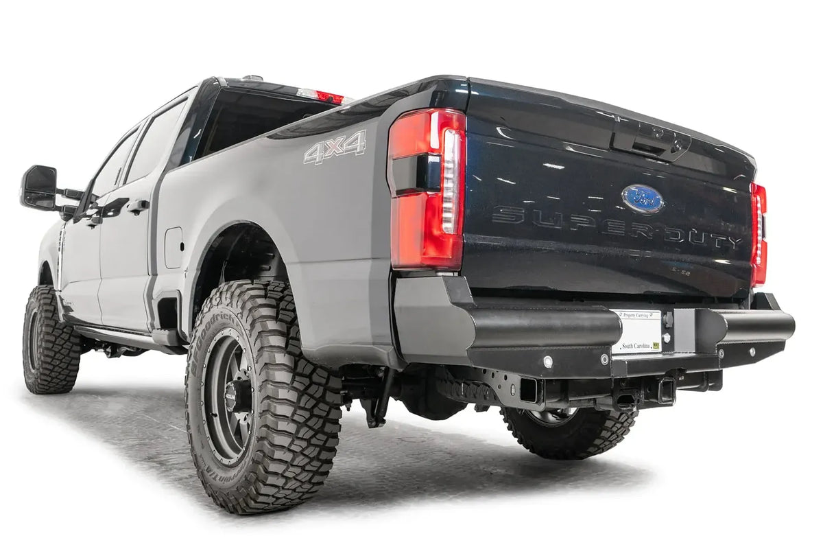 Fab Fours Black Steel Elite rear bumper on a gray and dark blue two-tone Ford Super Duty, rear driver-side three-quarter view, showing the smooth-plate tubular profile, wrapped corners and recessed plate mount
