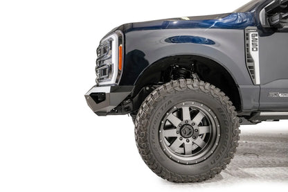 Fab Fours Vengeance front bumper on a dark blue Ford Super Duty, close-up of the driver-side corner, showing the bumper end profile, wheel-well clearance and lower skid section
