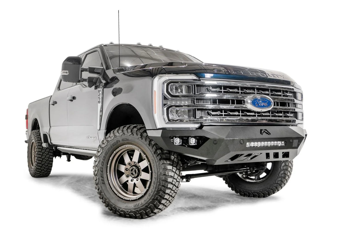 Fab Fours Vengeance front bumper on a gray and dark blue two-tone Ford Super Duty, front passenger-side three-quarter view, showing the angular bumper face, integrated LED light bar and cube light pockets
