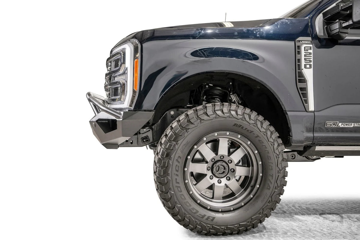 Fab Fours Vengeance front bumper with pre-runner guard on a dark blue Ford Super Duty, close-up of the driver-side corner, showing the pre-runner tube end, bumper wing and wheel-well clearance