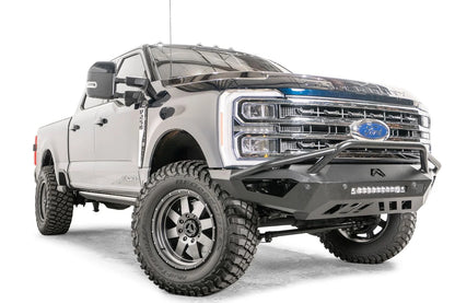 Fab Fours Vengeance front bumper with pre-runner guard on a gray and dark blue two-tone Ford Super Duty, front passenger-side three-quarter view, showing the pre-runner hoop, integrated LED light bar and angular skid section