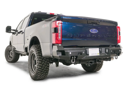 Fab Fours Premium rear bumper on a gray and dark blue two-tone Ford Super Duty, rear driver-side three-quarter view, showing the wrapped corners, D-ring shackle mounts and flush LED lights