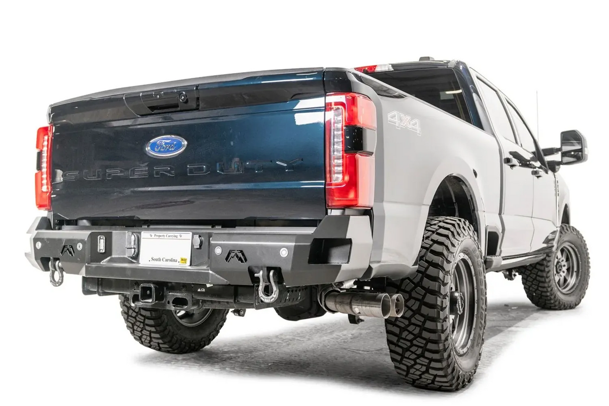 Fab Fours Premium rear bumper on a gray and dark blue two-tone Ford Super Duty, rear passenger-side three-quarter view, showing the sensor-retaining face, D-ring shackle mounts and flush LED lights