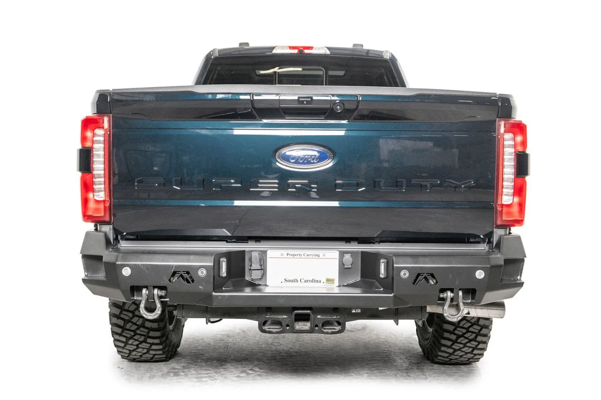 Fab Fours Premium rear bumper on a gray and dark blue two-tone Ford Super Duty, straight-on rear view, showing the sensor-retaining face, twin D-ring shackle mounts and center plate pocket