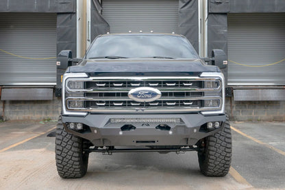 Fab Fours Matrix front bumper on a dark blue Ford Super Duty F-250 at a loading dock, straight-on front view, showing the no-guard winch bumper face, LED light bar and fairlead opening