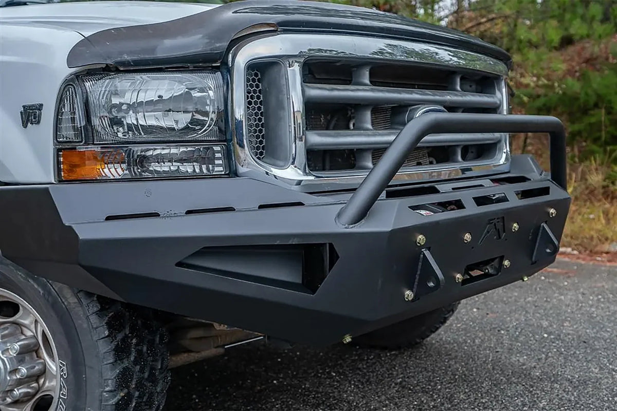 Fab Fours Red Steel front bumper with pre-runner guard on a white and tan two-tone Ford Super Duty F-250, outdoor close-up of the bumper face, showing the pre-runner tube, slotted top plate and bolted gusset detailing