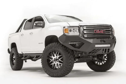 Fab Fours Vengeance front bumper on a white GMC Canyon, front driver-side three-quarter view, showing the sculpted no-guard face, LED light bar and angular skid section