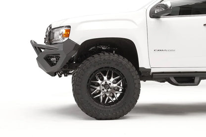 Fab Fours Vengeance front bumper with pre-runner guard on a white GMC Canyon, close-up of the driver-side corner, showing the pre-runner tube end, honeycomb light pocket and bumper wing