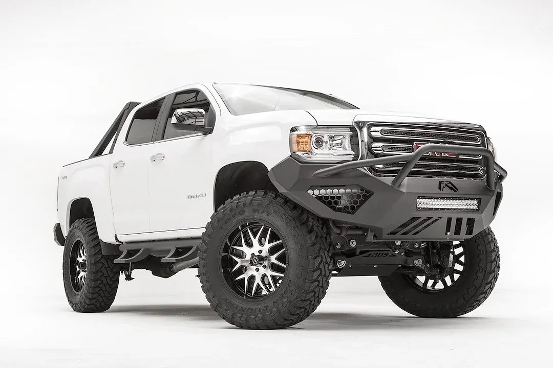 Fab Fours Vengeance front bumper with pre-runner guard on a white GMC Canyon, front driver-side three-quarter view, showing the pre-runner hoop, LED light bar and angular skid section