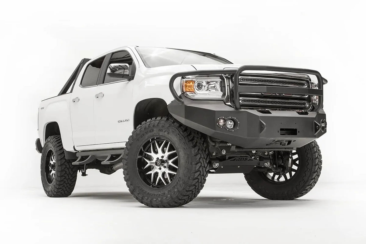 Fab Fours Premium front bumper with full guard on a white GMC Canyon, front driver-side three-quarter view, showing the full grille guard, winch opening and round fog light cutouts