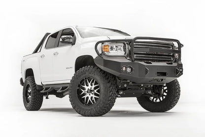Fab Fours Premium front bumper with full guard on a white GMC Canyon, front driver-side three-quarter view, showing the full grille guard, winch opening and round fog light cutouts