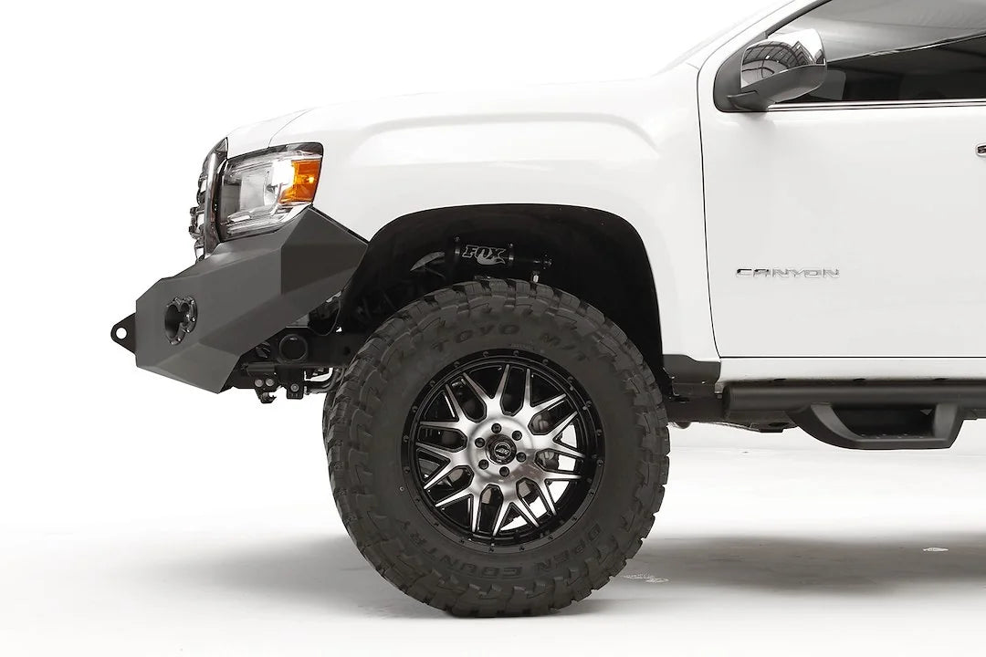 Fab Fours Premium front bumper on a white GMC Canyon, close-up of the driver-side corner, showing the bumper wing profile, shackle mount and wheel-well clearance