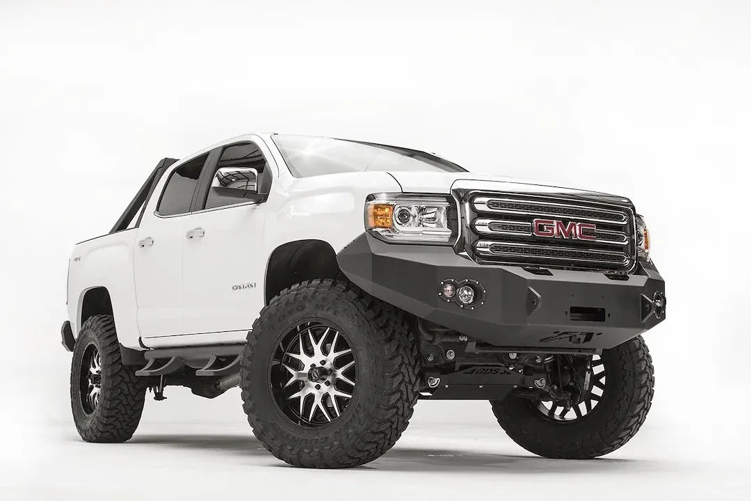 Fab Fours Premium front bumper on a white GMC Canyon, front driver-side three-quarter view, showing the no-guard winch bumper face, round fog light cutouts and wrapped wings