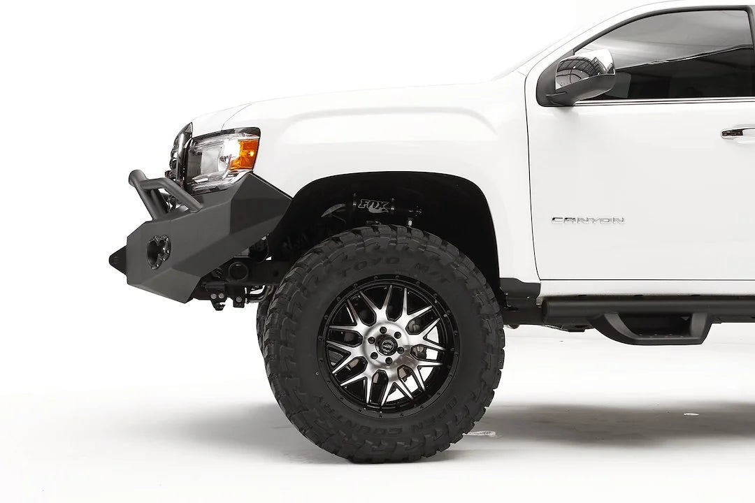 Fab Fours Premium front bumper with pre-runner guard on a white GMC Canyon, close-up of the driver-side corner, showing the pre-runner tube end, bumper wing and shackle mount