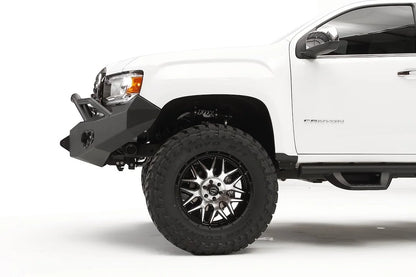 Fab Fours Premium front bumper with pre-runner guard on a white GMC Canyon, close-up of the driver-side corner, showing the pre-runner tube end, bumper wing and shackle mount