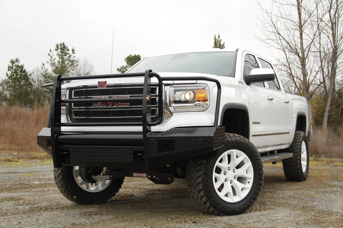 Fab Fours Black Steel front bumper with full guard on a white GMC Sierra 1500 parked on gravel, front driver-side three-quarter view, showing the full grille guard, mesh grille insert and diamond-plate bumper face