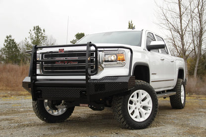 Fab Fours Black Steel front bumper with full guard on a white GMC Sierra 1500 parked on gravel, front driver-side three-quarter view, showing the full grille guard, mesh grille insert and diamond-plate bumper face