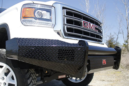 Fab Fours Black Steel front bumper on a white GMC Sierra 1500, outdoor close-up of the driver-side corner, showing the diamond-plate wing, honeycomb light opening and top tube