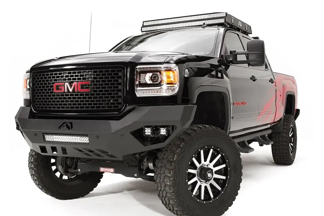 Fab Fours Vengeance front bumper on a black GMC Sierra 2500HD, front driver-side three-quarter view, showing the sculpted no-guard face, integrated LED light bar and cube light pockets