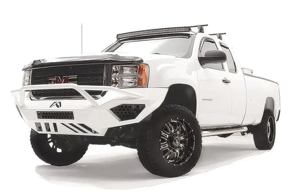 Fab Fours Vengeance front bumper with pre-runner guard on a white GMC Sierra 2500HD, front driver-side three-quarter view, showing the pre-runner hoop, honeycomb light pockets and slotted skid plate