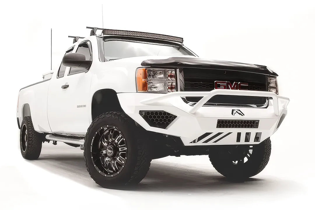 Fab Fours Vengeance front bumper with pre-runner guard on a white GMC Sierra 2500HD, front passenger-side three-quarter view, showing the pre-runner hoop, honeycomb light pockets and slotted skid plate