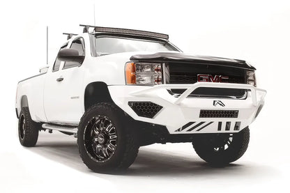 Fab Fours Vengeance front bumper with pre-runner guard on a white GMC Sierra 2500HD, front passenger-side three-quarter view, showing the pre-runner hoop, honeycomb light pockets and slotted skid plate