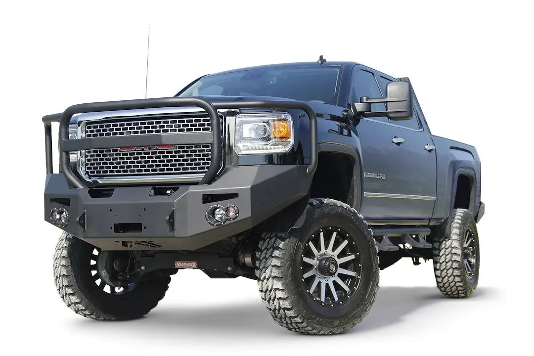 Fab Fours Premium Heavy Duty winch front bumper with full guard on a black GMC Sierra 2500HD, low outdoor close-up of the passenger-side corner, showing the guard hoop, winch fairlead opening and round fog light cutout