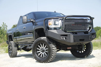 Fab Fours Premium Heavy Duty winch front bumper with full guard on a black GMC Sierra 2500HD parked on gravel, front passenger-side three-quarter view, showing the grille guard hoop, winch opening and fog light cutouts