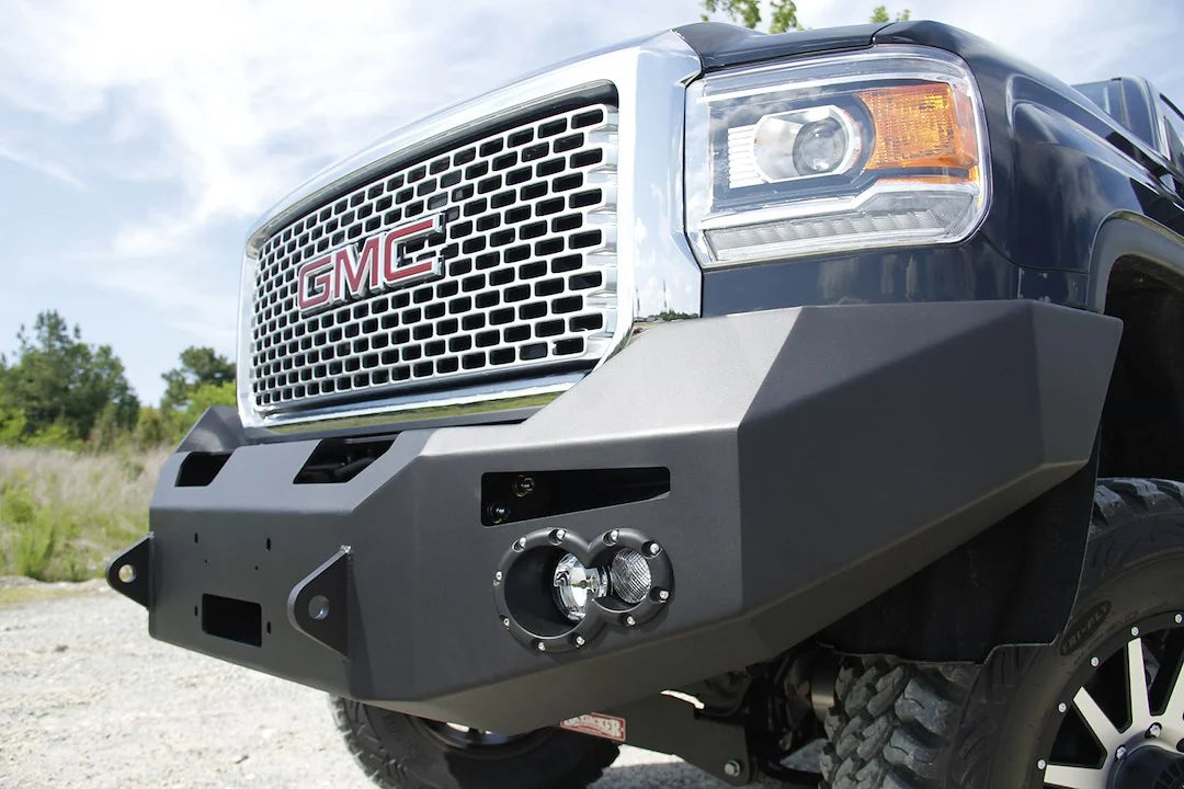 Fab Fours Premium Heavy Duty winch front bumper on a black GMC Sierra 2500HD, outdoor close-up of the passenger-side corner, showing the faceted bumper wing, round fog light cutout and shackle tab