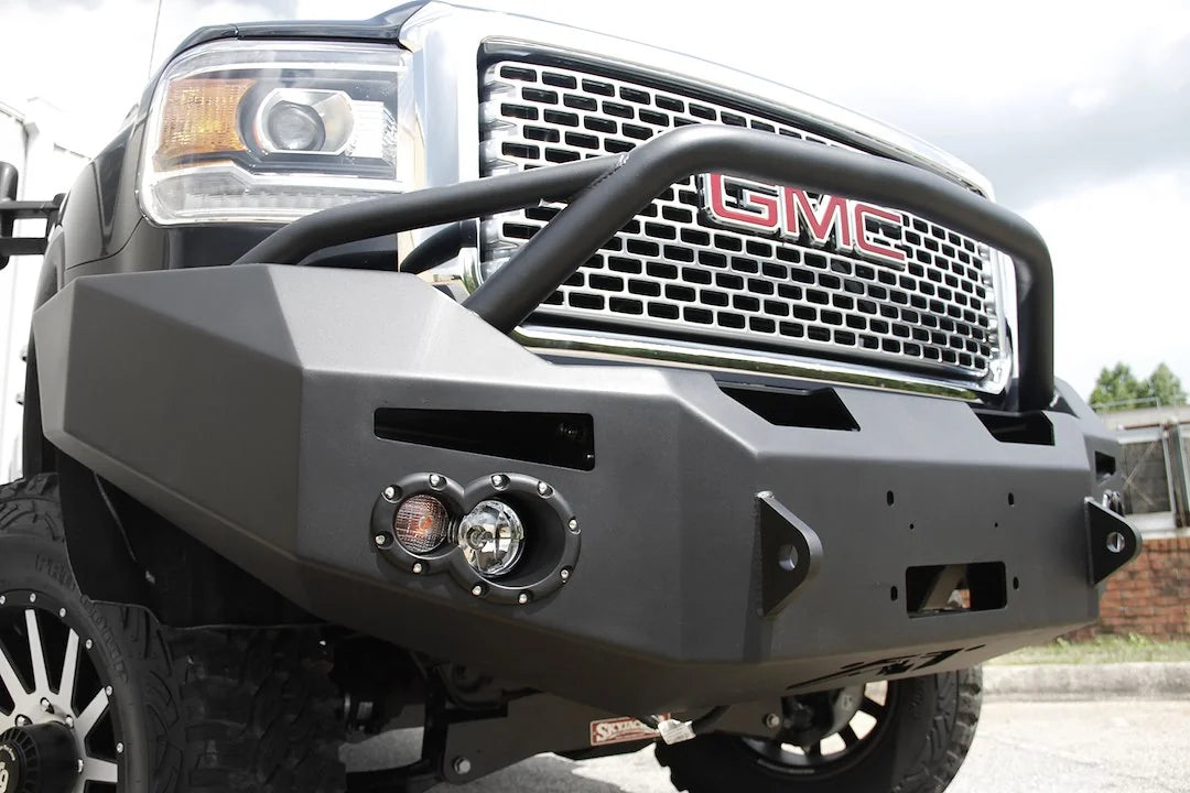 Fab Fours Premium Heavy Duty winch front bumper with pre-runner guard on a black GMC Sierra 2500HD, outdoor close-up of the passenger-side corner, showing the pre-runner tube, round fog light cutouts and shackle tab