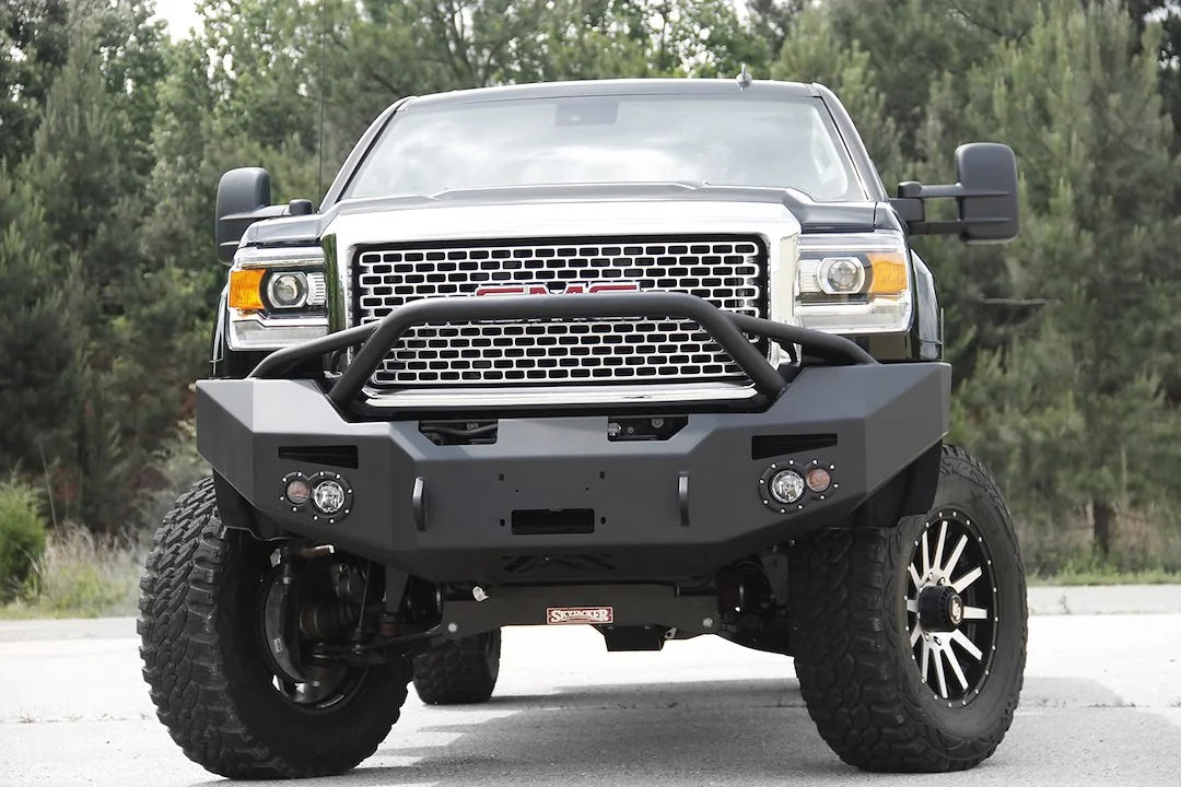Fab Fours Premium Heavy Duty winch front bumper with pre-runner guard on a black GMC Sierra 2500HD, straight-on front outdoor view, showing the pre-runner hoop, center winch opening and round fog light cutouts