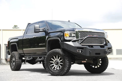 Fab Fours Premium Heavy Duty winch front bumper with pre-runner guard on a black GMC Sierra 2500HD parked outside a building, front passenger-side three-quarter view, showing the pre-runner hoop, winch opening and round fog light cutouts