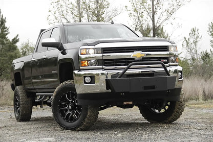 Fab Fours winch mount with pre-runner guard on a black Chevrolet Silverado 2500HD parked on gravel, front passenger-side three-quarter view, showing the pre-runner hoop, winch plate and factory bumper integration