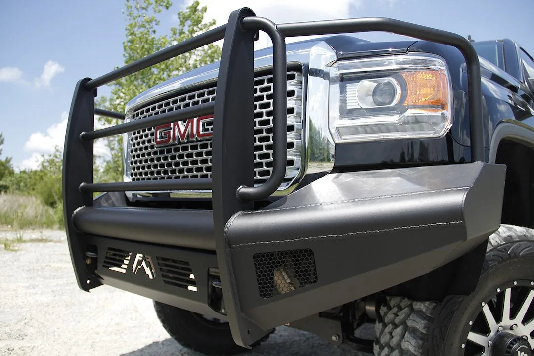 Fab Fours Black Steel Elite front bumper with full guard on a black GMC Sierra 2500HD, low outdoor close-up of the driver-side corner, showing the guard uprights, headlight hoop and mesh light opening