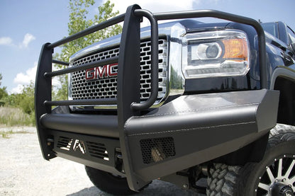 Fab Fours Black Steel Elite front bumper with full guard on a black GMC Sierra 2500HD, low outdoor close-up of the driver-side corner, showing the guard uprights, headlight hoop and mesh light opening