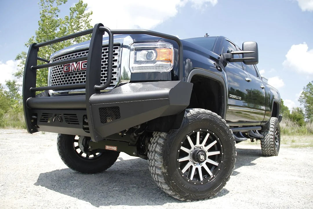 Fab Fours Black Steel Elite front bumper with full guard on a black GMC Sierra 2500HD parked on gravel, front driver-side three-quarter view, showing the full grille guard, smooth-plate face and mesh light openings