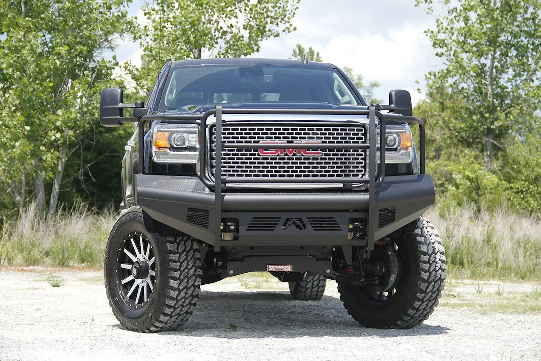 Fab Fours Black Steel Elite front bumper with full guard on a black GMC Sierra 2500HD parked on gravel, straight-on front view, showing the full grille guard hoops, smooth-plate bumper face and mesh light openings