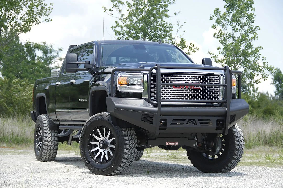 Fab Fours Black Steel Elite front bumper with full guard on a black GMC Sierra 2500HD parked on gravel, front passenger-side three-quarter view, showing the full grille guard, smooth-plate face and wrapped wings