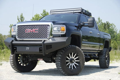 Fab Fours Black Steel Elite front bumper on a black GMC Sierra 2500HD parked on gravel, front driver-side three-quarter view, showing the no-guard smooth-plate face, top tube and mesh light openings