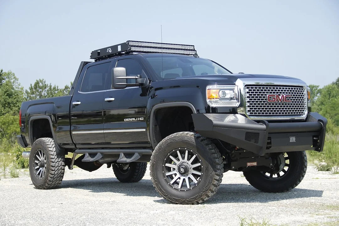 Fab Fours Black Steel Elite front bumper on a black GMC Sierra 2500HD parked on gravel, front passenger-side three-quarter view, showing the no-guard smooth-plate face, top tube and wrapped wings