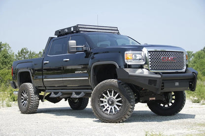 Fab Fours Black Steel Elite front bumper on a black GMC Sierra 2500HD parked on gravel, front passenger-side three-quarter view, showing the no-guard smooth-plate face, top tube and wrapped wings