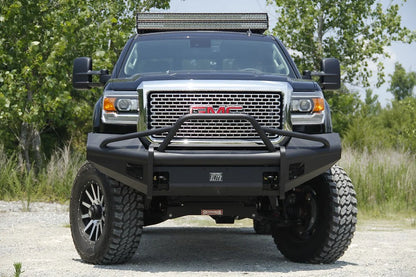 Fab Fours Black Steel Elite front bumper with pre-runner guard on a black GMC Sierra 2500HD parked on gravel, straight-on front view, showing the pre-runner hoop, Elite badge and mesh light openings