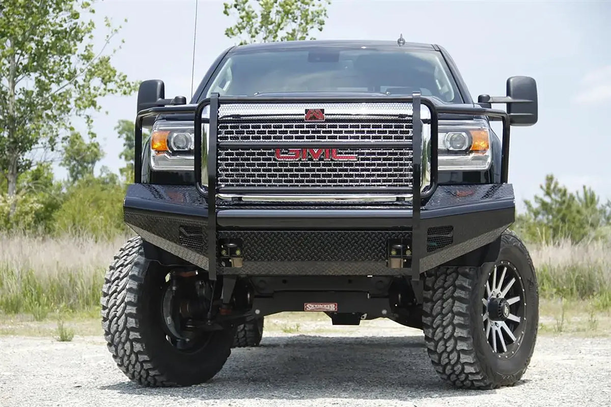 Fab Fours Black Steel front bumper with full guard on a black GMC Sierra 2500HD parked on gravel, straight-on front view, showing the full grille guard hoops, mesh grille insert and diamond-plate bumper face