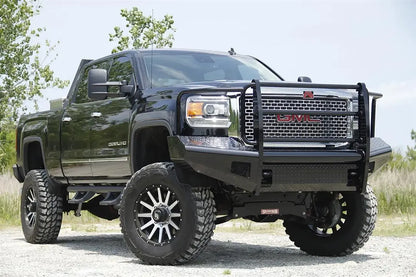 Fab Fours Black Steel front bumper with full guard on a black GMC Sierra 2500HD parked on gravel, front passenger-side three-quarter view, showing the full grille guard, headlight hoops and diamond-plate wings