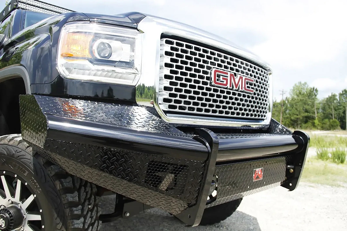 Fab Fours Black Steel front bumper on a black GMC Sierra 2500HD, low outdoor close-up of the passenger-side corner, showing the diamond-plate wing, honeycomb light opening and top tube
