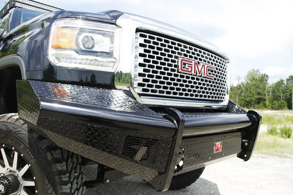 Fab Fours Black Steel front bumper on a black GMC Sierra 2500HD, low outdoor close-up of the passenger-side corner, showing the diamond-plate wing, honeycomb light opening and top tube