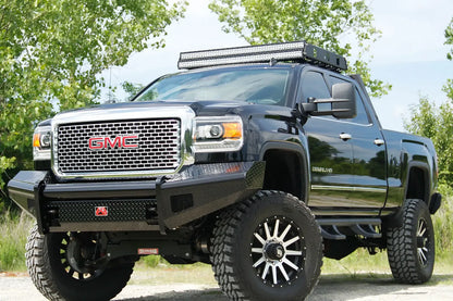 Fab Fours Black Steel front bumper on a black GMC Sierra 2500HD parked on gravel, front driver-side three-quarter view, showing the no-guard diamond-plate face, top tube and wrapped wings
