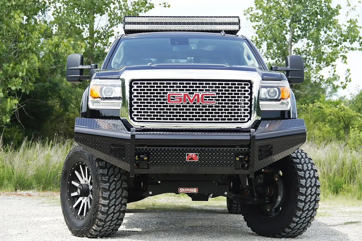 Fab Fours Black Steel front bumper on a black GMC Sierra 2500HD parked on gravel, straight-on front view, showing the no-guard diamond-plate face, top tube and center logo plate